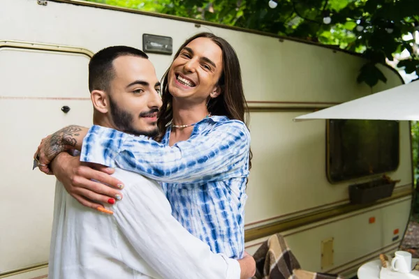 Happy tattooed gay man hugging cheerful boyfriend near travel van — Photo de stock