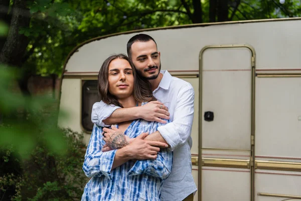 Barbudo gay hombre abrazando tatuado novio cerca de viaje van - foto de stock