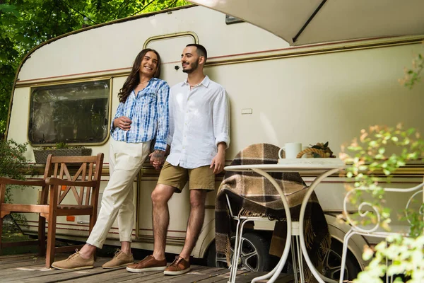 Full length view of happy gay couple holding hands while standing near van while camping together — Photo de stock