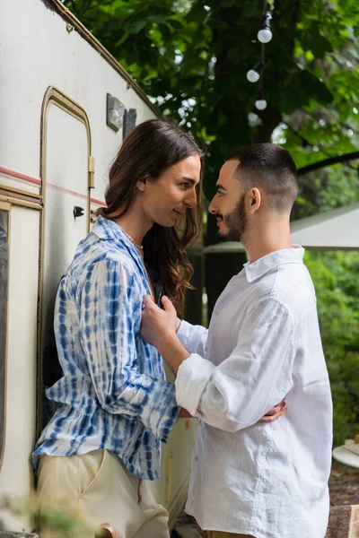 Side view of happy gay couple smiling while hugging during journey near van — Stock Photo