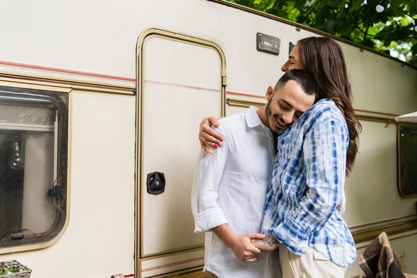 Happy gay couple smiling while hugging and holding hands during journey near van — Stock Photo