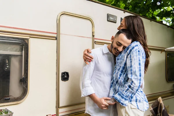 Happy gay couple smiling while hugging and holding hands during journey near van — Fotografia de Stock