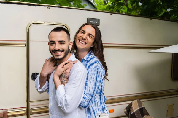 Glückliches homosexuelles Paar lächelt, während es sich umarmt und in die Kamera in der Nähe eines Lieferwagens schaut — Stockfoto