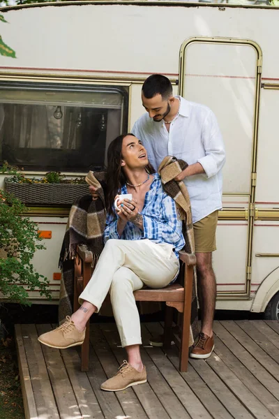 Fürsorglicher schwuler Mann hält Decke in der Nähe von Partner mit Tasse Kaffee in der Nähe von Lieferwagen — Stockfoto