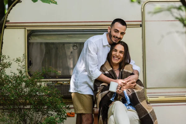 Barbu gay homme câlin heureux copain dans couverture assis avec tasse de café près de van — Photo de stock