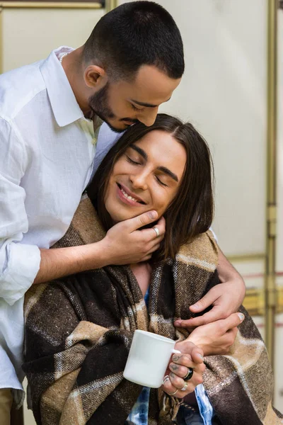 Caring gay man hugging happy boyfriend in blanket sitting near van — Fotografia de Stock