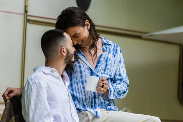 Happy tattooed gay man holding cup of coffee near bearded boyfriend and travel van — Photo de stock