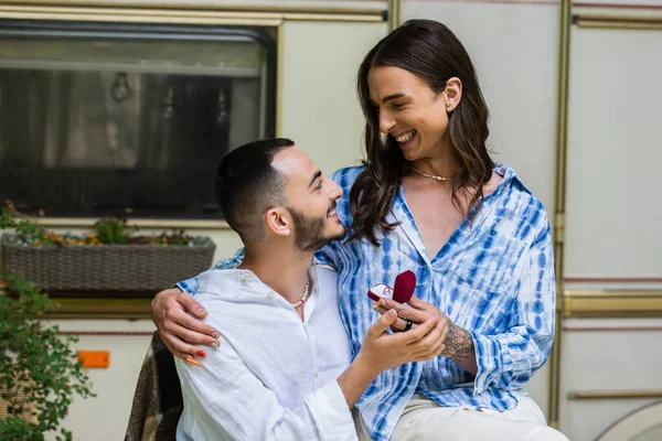 Schwuler Mann macht Heiratsantrag, während er Schmuckschatulle mit Ring in der Nähe von glücklichem Freund und Lieferwagen hält — Stockfoto