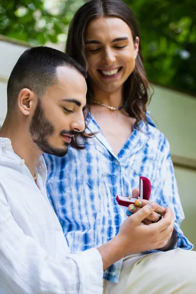 Glücklicher schwuler Mann macht Heiratsantrag, während er im Sommer Schmuckschatulle mit Ring in der Nähe seines Freundes hält — Stockfoto