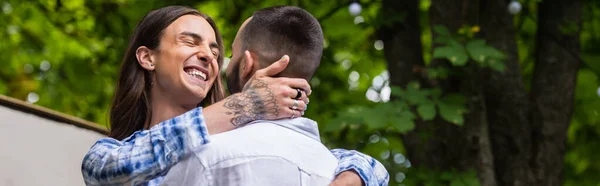 Hombre gay tatuado sonriendo y abrazando novio en verano, pancarta - foto de stock