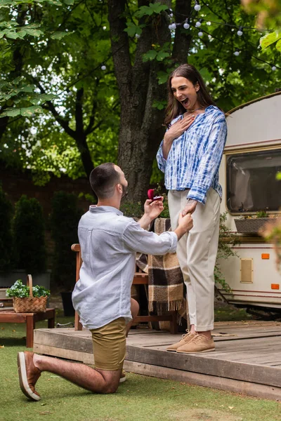 Gay man making proposal while holding jewelry box with ring near surprised boyfriend during journey in summer — Stock Photo