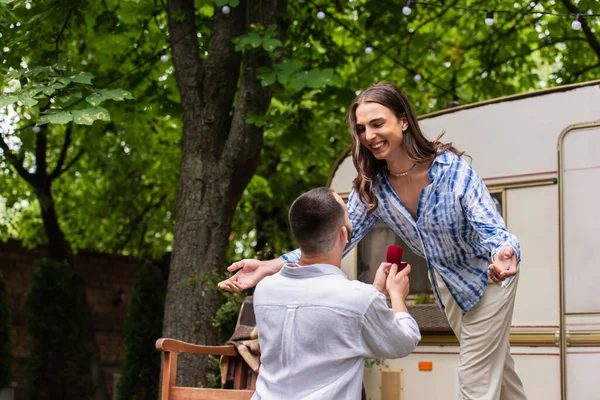 Гей чоловік робить пропозицію, тримаючи ювелірну коробку з кільцем біля щасливого хлопця під час подорожі влітку — стокове фото