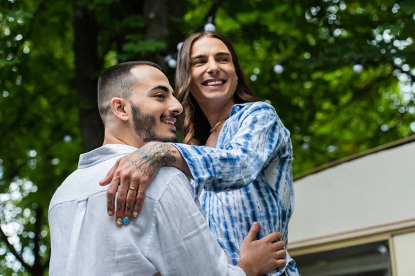 Низкий угол обзора женатой гей-пары, улыбающейся, обнимаясь возле фургона — стоковое фото