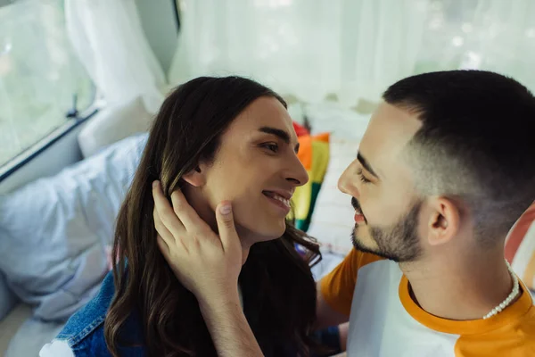 Gay hombre con largo cabello mirando sonriente barbudo novio en van - foto de stock