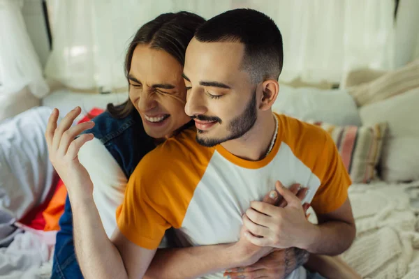 Vue grand angle de sourire gay homme avec tatouage étreignant copain barbu avec les yeux fermés dans van moderne — Photo de stock