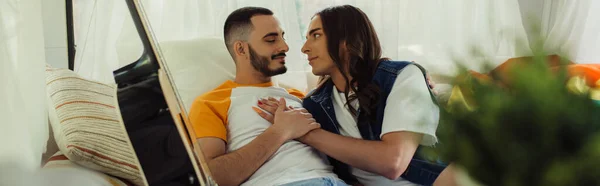 Gay man with long hair hugging bearded boyfriend on bed near guitar in modern van, banner — Foto stock