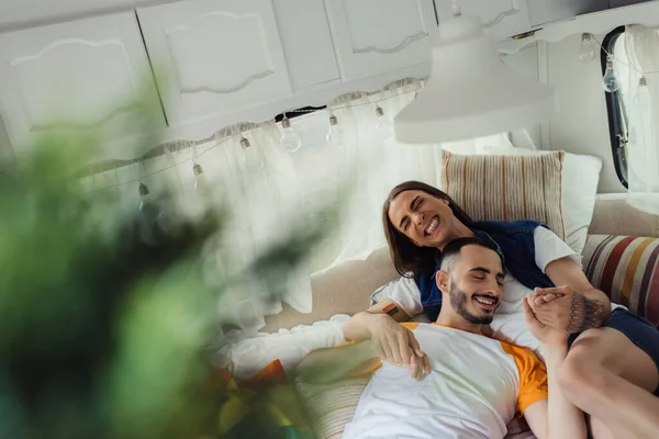 Smiling and tattooed gay man hugging bearded boyfriend on bed in modern van — Stock Photo