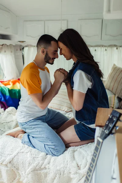 Seitenansicht eines schwulen Mannes mit Tätowierung, der Hände mit einem bärtigen Freund auf dem Bett in einem Lieferwagen hält — Stockfoto