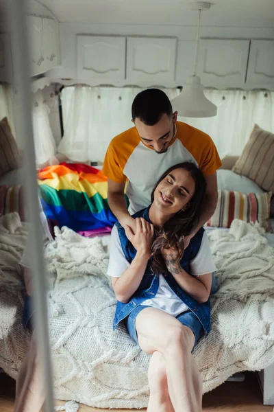 Gay man hugging pleased boyfriend with tattoo sitting on bed in van — Stockfoto