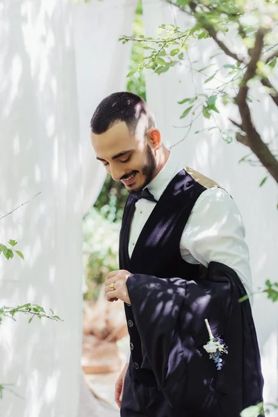 Щасливий бородатий наречений в офіційному одязі дивиться на золоте весільне кільце на пальці — стокове фото