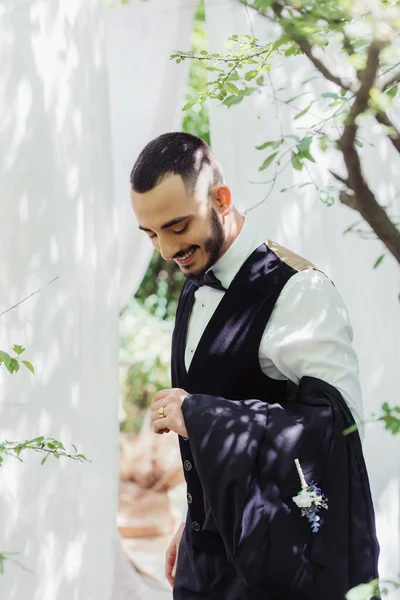 Happy bearded groom in formal wear looking at golden wedding ring on finger — Stockfoto