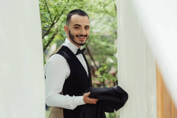 Happy groom holding blazer in hands while standing outside — Photo de stock