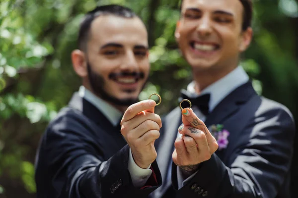 Happy and blurred gay men holding wedding rings in hands - foto de stock