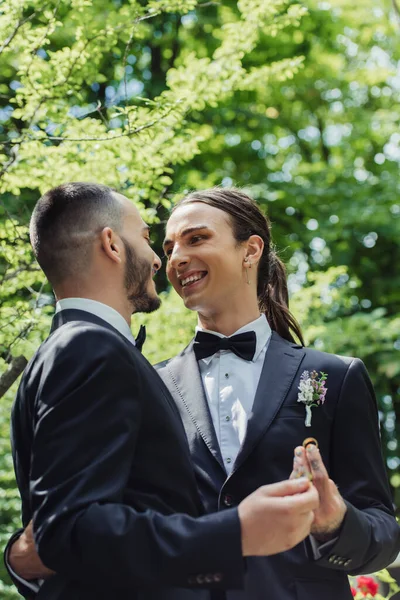 Happy gay couple in formal wear holding golden wedding rings in hands — Stock Photo
