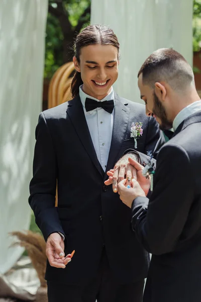 Bearded gay man wearing wedding ring on finger of cheerful tattooed groom — Photo de stock