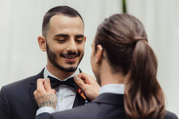 Tattooed gay man adjusting bow tie on suit of happy bearded groom — Foto stock