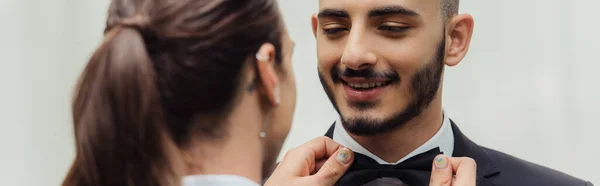 Tattooed gay man adjusting bow tie on suit of happy bearded groom, banner - foto de stock