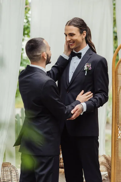 Bärtiger schwuler Mann berührt am Hochzeitstag die Wange eines zufriedenen Bräutigams — Stockfoto