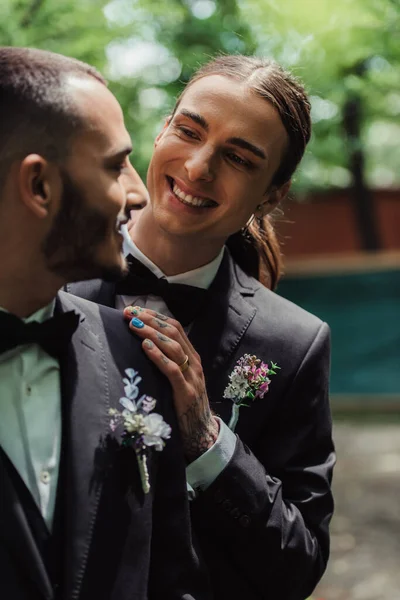Счастливые молодожёны-геи в костюмах с бутоньерками, смотрящими друг на друга — стоковое фото