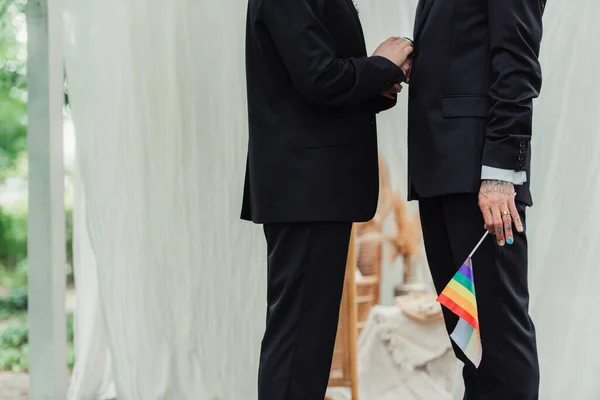 Partial view of tattooed gay man with wedding ring holding lgbt flag near groom — Stockfoto