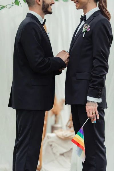 Cropped view of happy gay newlyweds in formal wear with lgbt flag during wedding ceremony — Foto stock