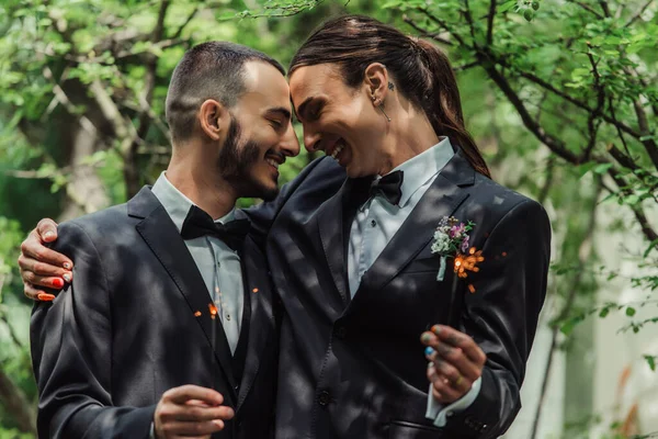 Smiling gay couple in formal wear holding sparklers in green park on wedding day — Foto stock