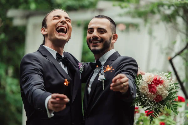 Excited gay couple in formal wear holding sparklers on wedding day — Photo de stock