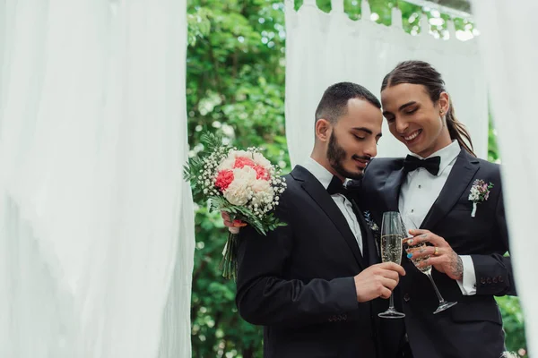 Lächelndes schwules Paar in Anzügen, das am Hochzeitstag Sektgläser klappert — Stockfoto