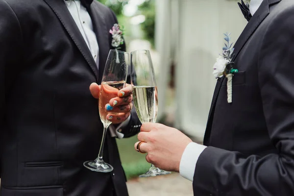 Cropped view of gay newlyweds in suits holding glasses with champagne on wedding day — Stock Photo