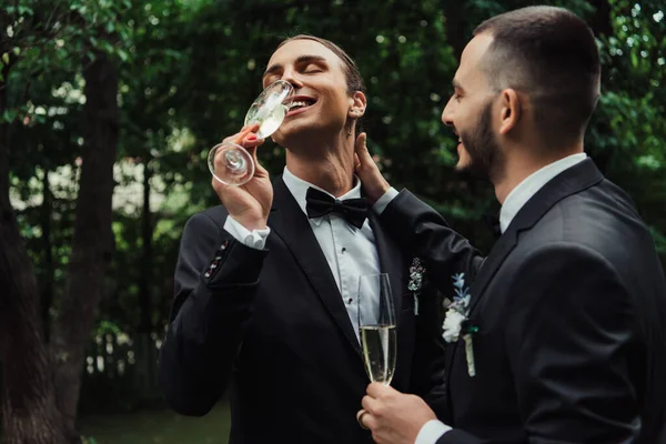 Happy gay newlyweds in suits drinking champagne on wedding day — Stock Photo