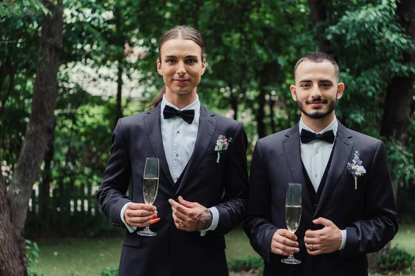 Schwule Brautpaare in Anzügen halten am Hochzeitstag Gläser mit Champagner in der Hand — Stockfoto
