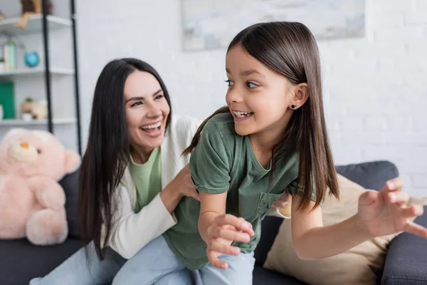 Feliz morena mujer jugando con alegre chica en sala de estar - foto de stock