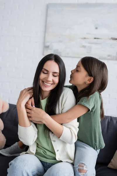 Bruna ragazza con gli occhi chiusi baciare felice babysitter in soggiorno — Foto stock