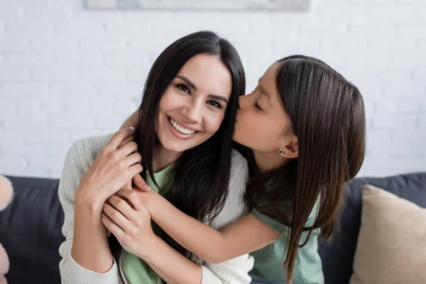 Brunette girl with closed eyes kissing cheek of happy babysitter in living room — Stock Photo