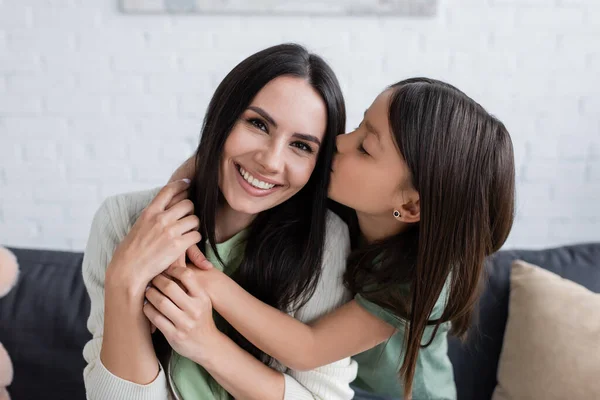 Brunette girl with closed eyes kissing cheek of happy babysitter in living room — Stockfoto