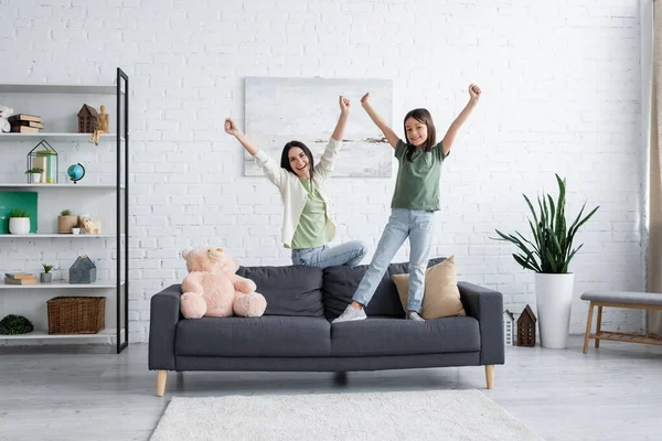 Excited babysitter and girl with outstretched hands in modern living room - foto de stock
