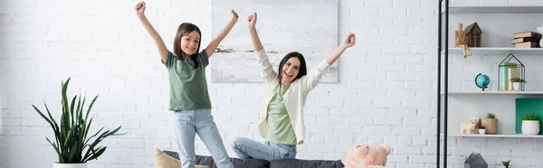 Mujer y chica emocionadas con las manos extendidas en la sala de estar moderna, pancarta - foto de stock