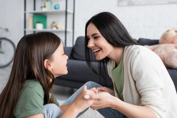 Babysitter sorridente e felice ragazza che si tiene per mano mentre si guarda a vicenda a casa — Foto stock