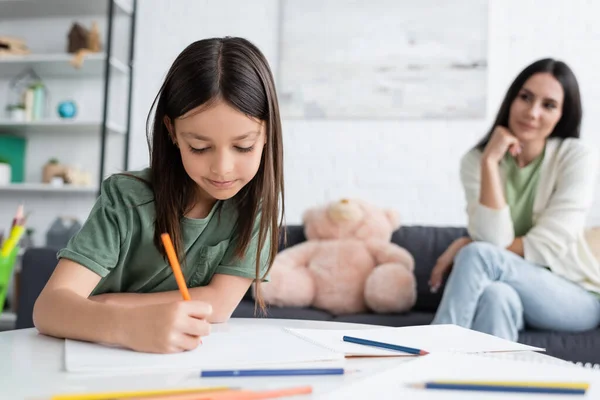 Happy girl drawing on paper near blurred babysitter on background — Foto stock