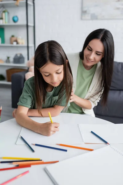 Happy babysitter looking at girl drawing on paper at home — Fotografia de Stock